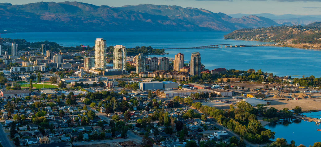 A scenic view of Kelowna, BC, showcasing the city skyline with Okanagan Lake and mountains in the background