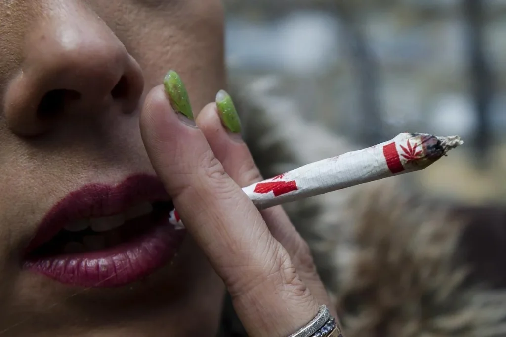 Close-up of a person smoking a cannabis joint wrapped in Canadian-themed paper.