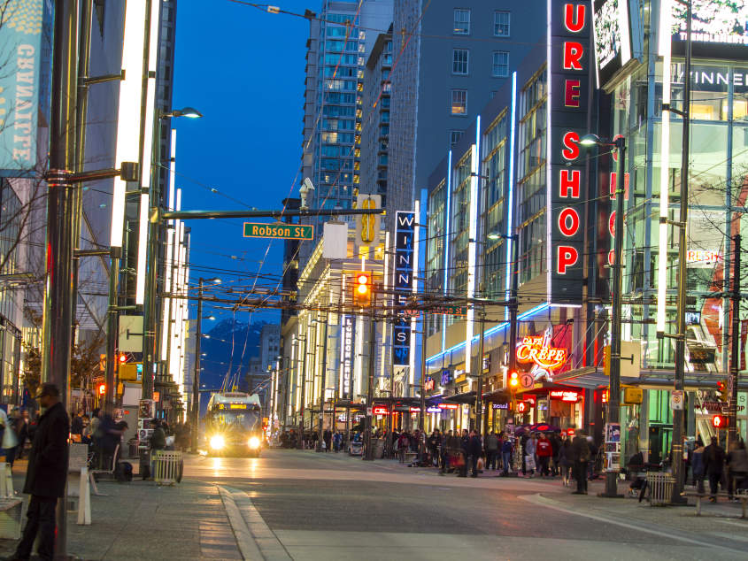 Robson Street in Vancouver, BC at night with busy shops and lights.